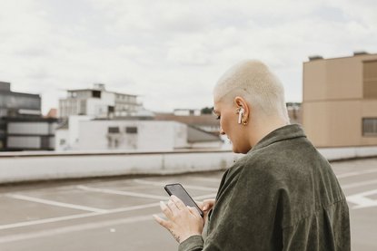 Frau mit Wireless Kopfhörern hält ein Handy in ihren Händen