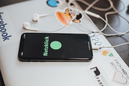 Smartphone mit Schriftzg "Netzklick" auf dem Display liegt auf einem Laptop.
